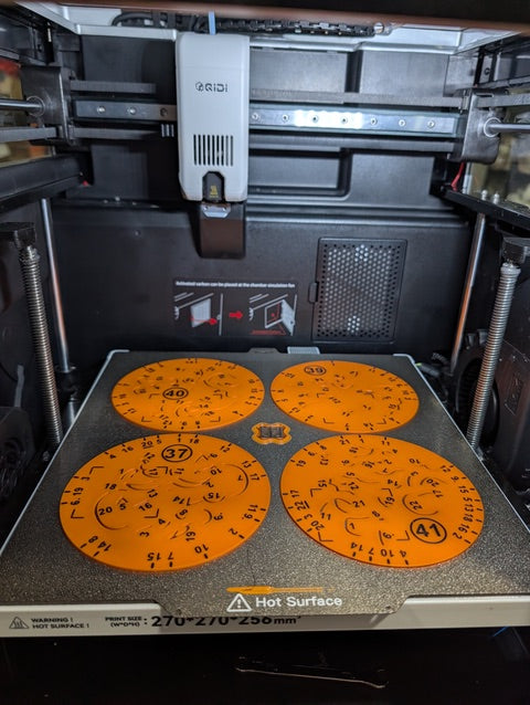 Orange circular 3D‑printed dial parts being printed on RIDI FDM 3D‑printer build plate