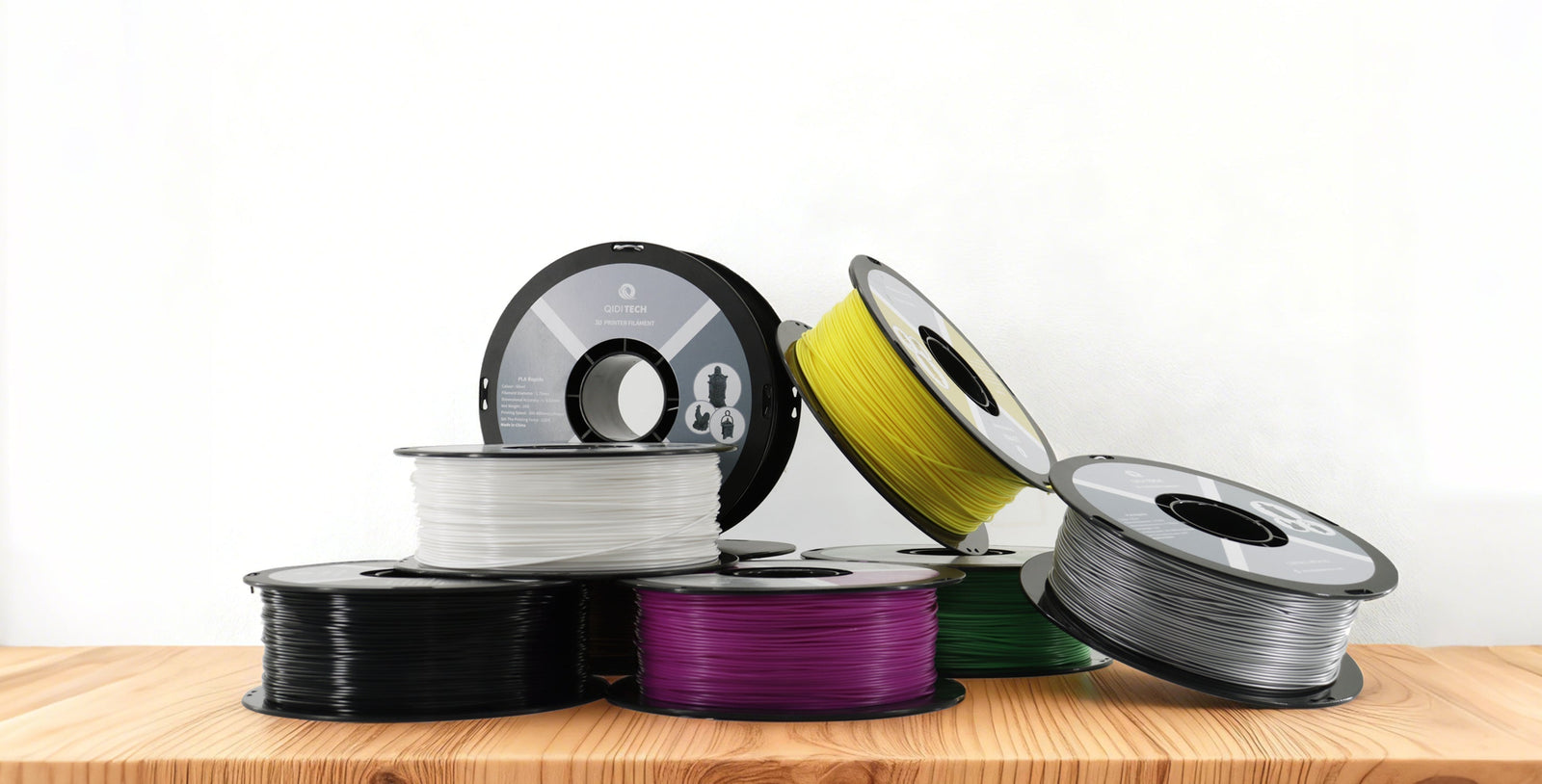 An assortment of colorful 3D printer filament spools, including yellow, purple, and white, on a wood table against a white background